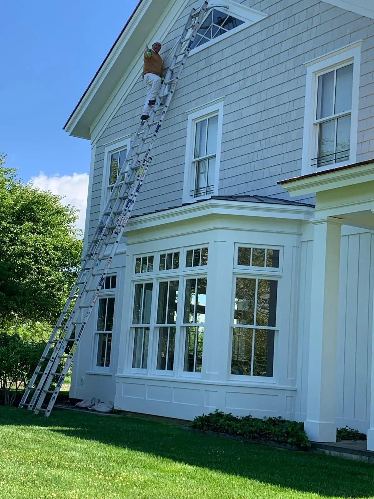 Painter on a ladder repainting a home's upper trim in East Hampton, NY
