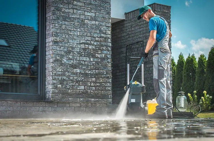 Pressure washing a stone patio next to a home